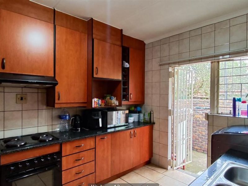 Functional kitchen featuring wood-finish cabinetry, dark countertops, built-in oven and hob, and direct access to the rear exterior through a security gate.