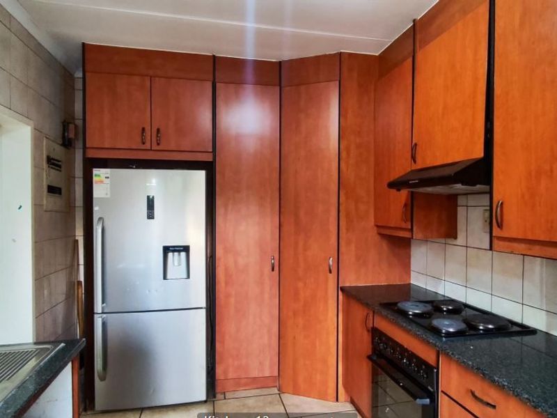 A functional kitchen featuring wood-finish cabinetry, granite countertops, a built-in oven with hob, and an extractor fan, with tiled splashbacks and flooring.