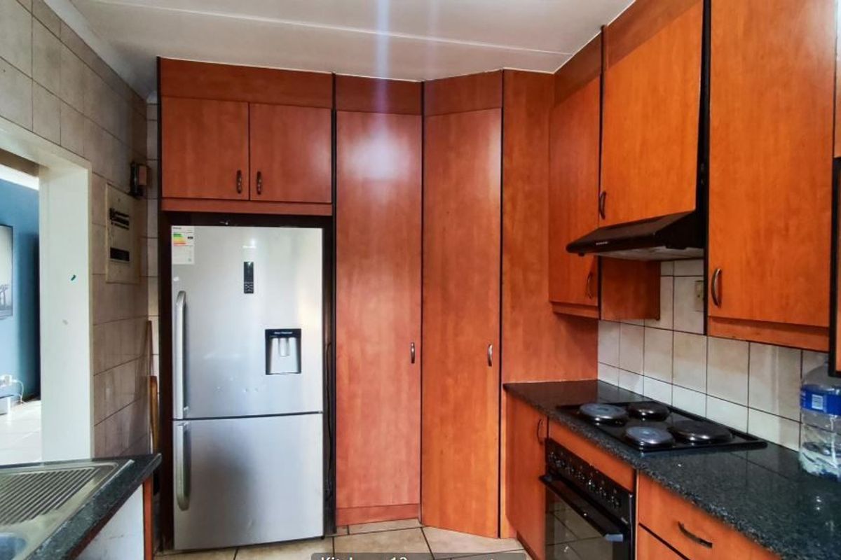 A functional kitchen featuring wood-finish cabinetry, granite countertops, a built-in oven with hob, and an extractor fan, with tiled splashbacks and flooring.