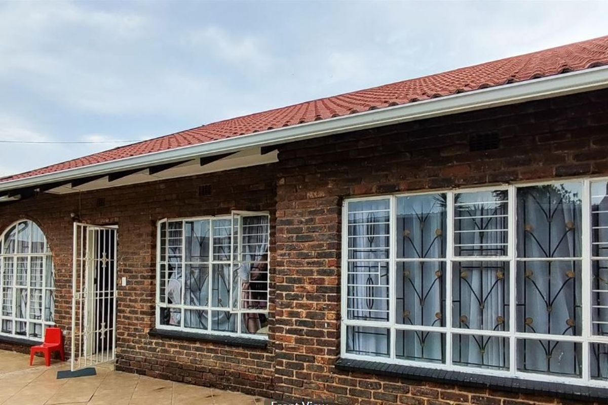 A rear view of the townhouse featuring a face brick facade, tiled roof, and a paved patio area with security bars on the windows.
