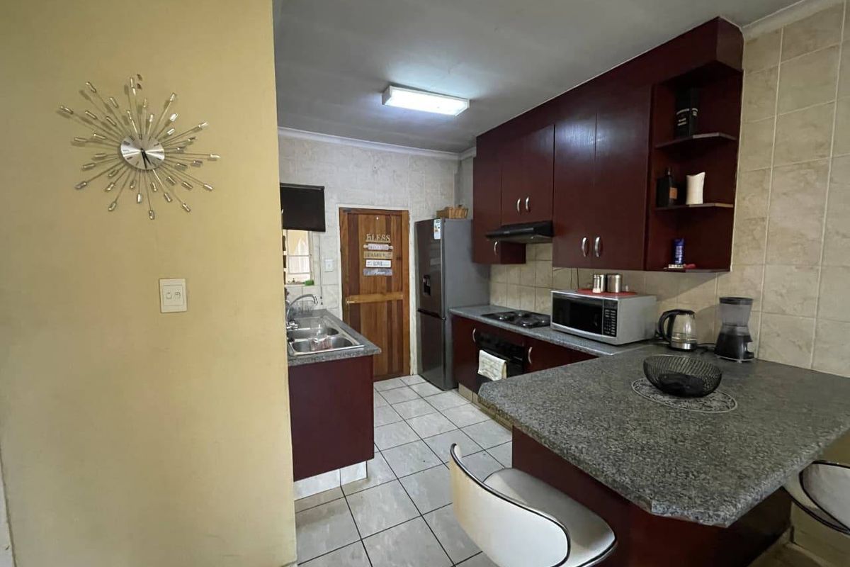 A functional kitchen featuring dark wood cabinetry, granite-look countertops, a breakfast bar, and tiled flooring, providing a practical layout for daily meal preparation.