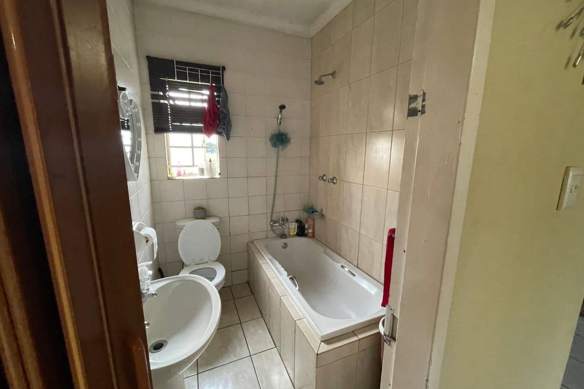 A compact bathroom featuring a built-in bathtub with shower attachment, pedestal basin, and toilet, finished with neutral wall and floor tiling.