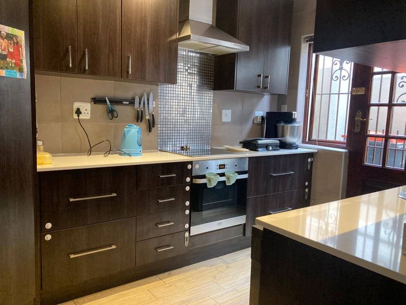 A functional kitchen featuring dark wood cabinetry, stone countertops, a built-in oven with electric hob, and a modern mosaic tile splashback.