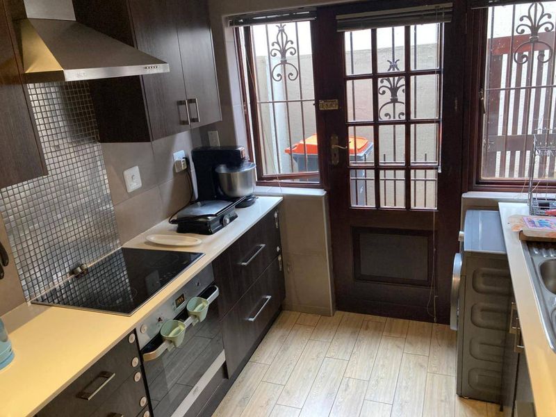 Compact kitchen featuring dark wood cabinetry, mosaic tile backsplash, integrated electric hob and oven, and direct access to an exterior area.