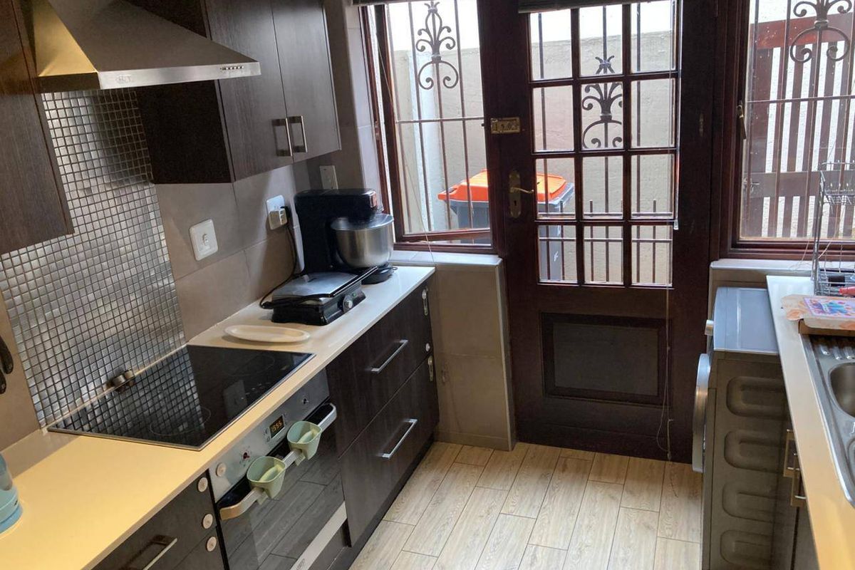 Compact kitchen featuring dark wood cabinetry, mosaic tile backsplash, integrated electric hob and oven, and direct access to an exterior area.