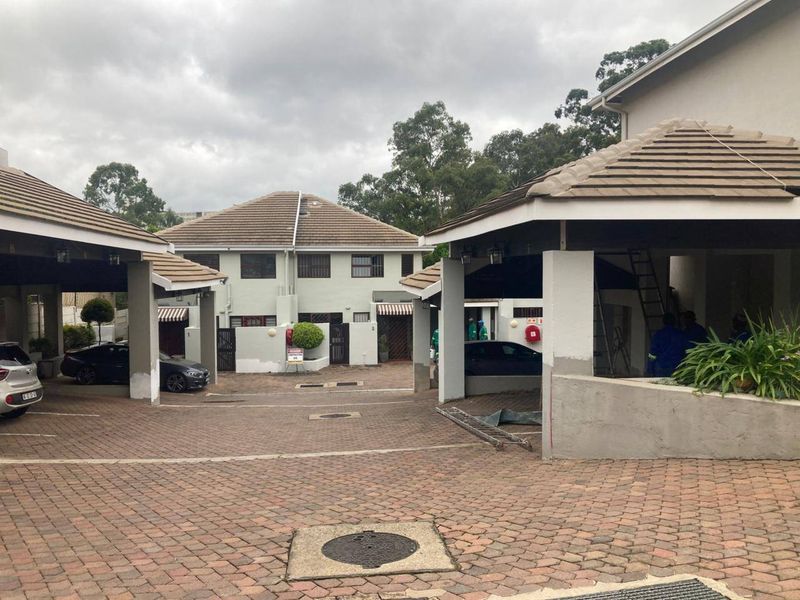 Front view of an apartment complex featuring paved driveway access and covered parking bays with ongoing exterior maintenance visible.