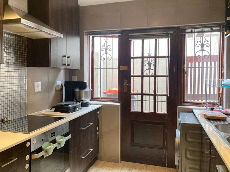 A functional kitchen featuring dark cabinetry, a mosaic tile backsplash, integrated oven and hob, and direct access to an exterior area via a timber door.