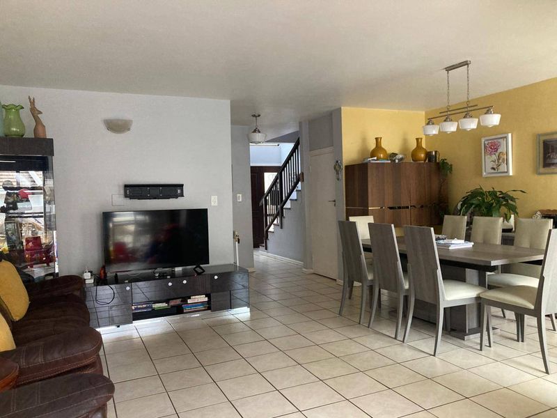 Open-plan living and dining area featuring tiled flooring, a central staircase, and neutral wall finishes with a feature wall.