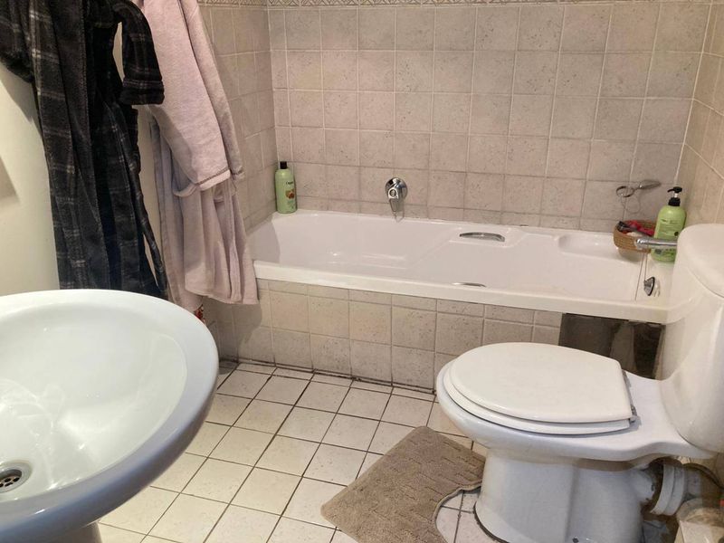 A functional bathroom featuring a standard bathtub, pedestal basin, and toilet with neutral ceramic tiling throughout.