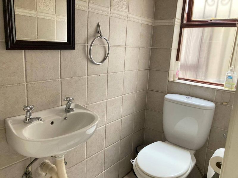 A compact bathroom featuring neutral ceramic wall tiles, a pedestal basin, and a standard dual-flush toilet with a frosted glass window.