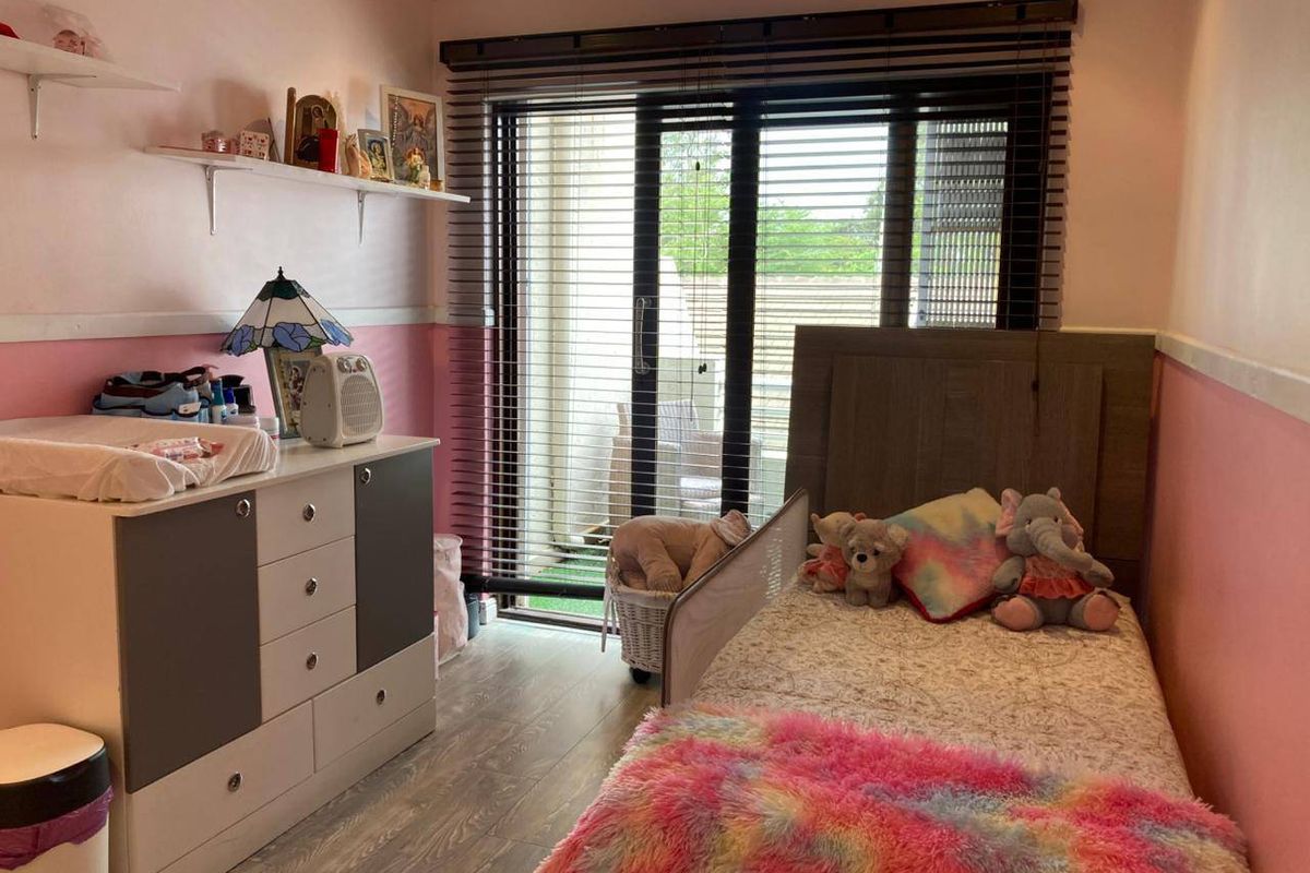 A bedroom featuring laminate flooring, wall-mounted shelving, and a sliding glass door with venetian blinds providing access to an outdoor area.