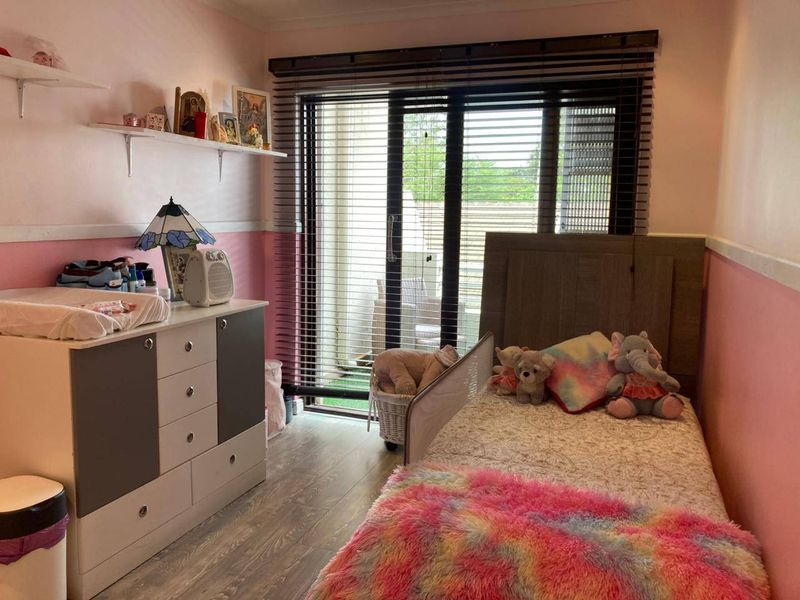 A bedroom featuring laminate flooring, wall-mounted shelving, and a sliding glass door with venetian blinds providing access to an outdoor area.