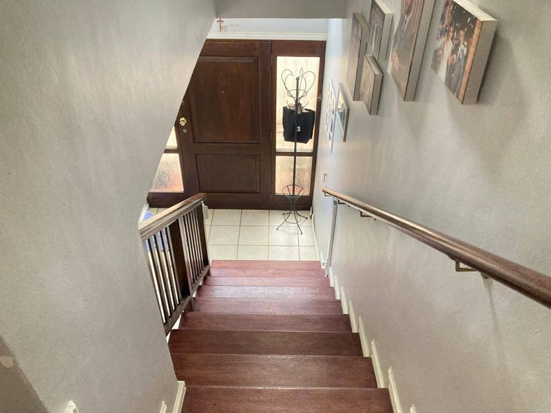 An interior view looking down a wooden staircase towards the main entrance, featuring a timber front door and tiled flooring.