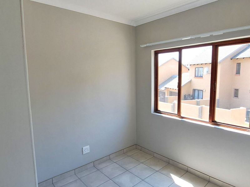 A bright, empty bedroom featuring neutral wall paint, tiled flooring, and a large window with a wooden frame.