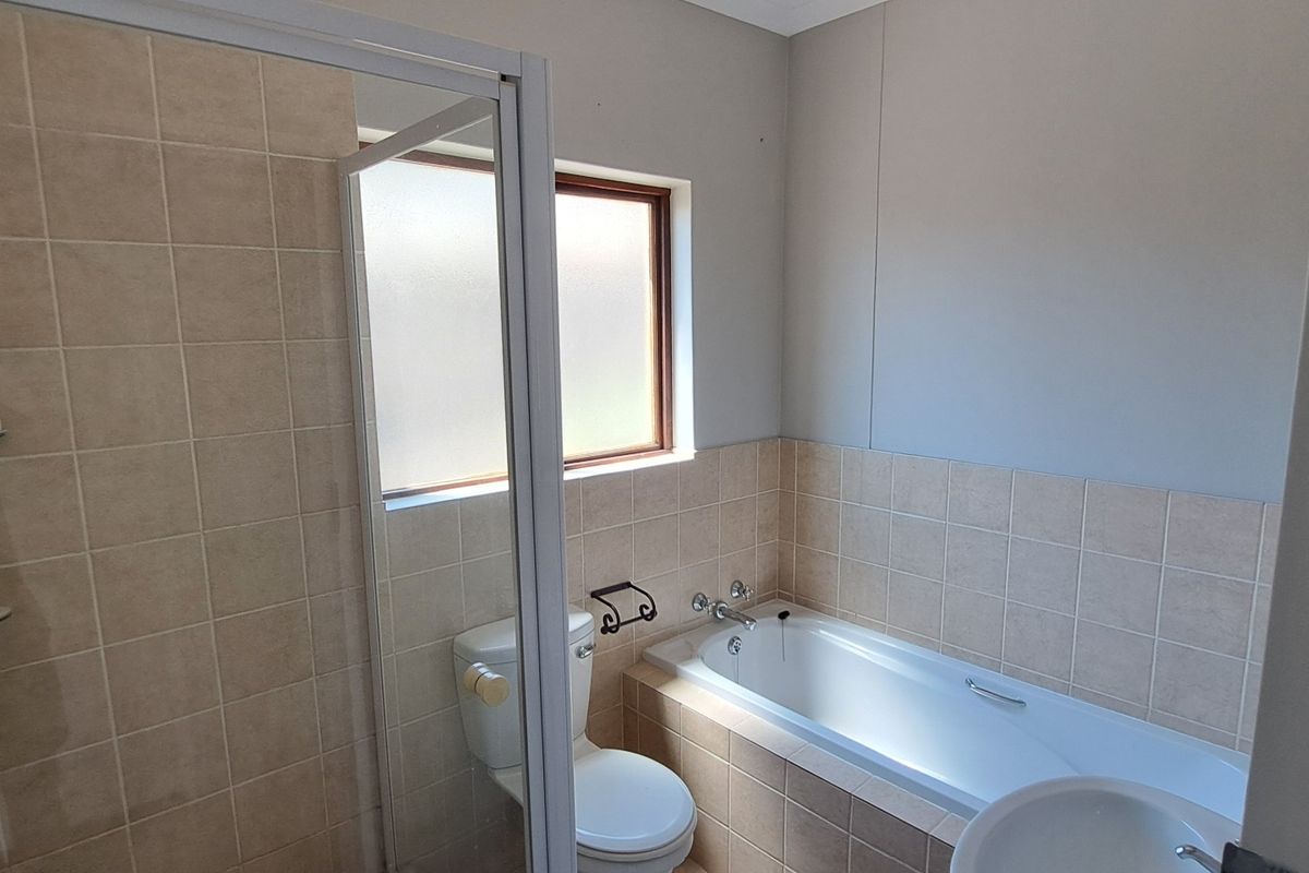 A functional bathroom featuring a separate shower enclosure, bathtub, toilet, and basin with neutral wall tiling.