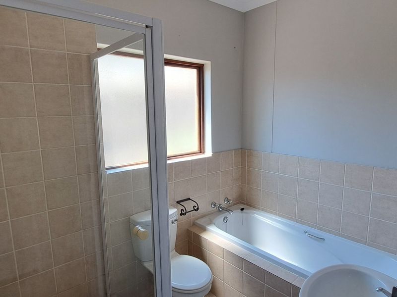 A functional bathroom featuring a separate shower enclosure, bathtub, toilet, and basin with neutral wall tiling.