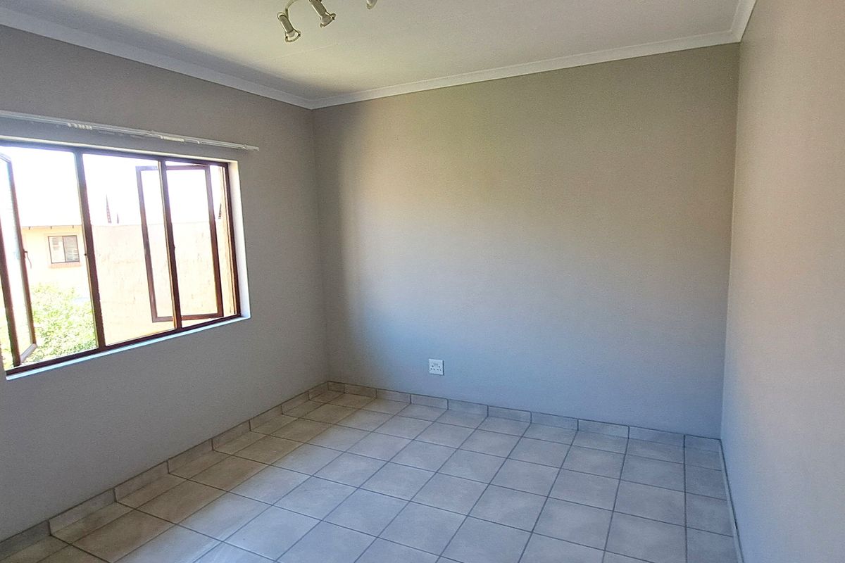 A clean, empty bedroom featuring neutral wall paint, tiled flooring, and a casement window providing natural light.