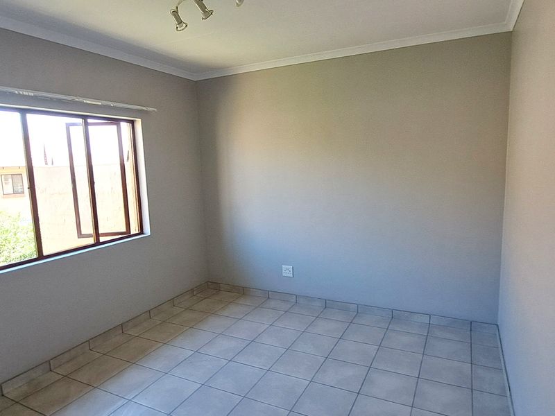 A clean, empty bedroom featuring neutral wall paint, tiled flooring, and a casement window providing natural light.