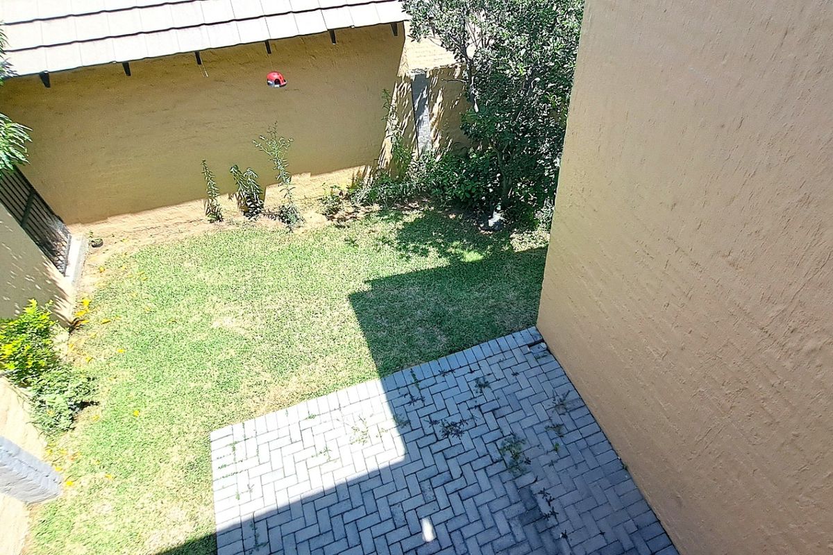 An elevated view of a private rear garden featuring a paved patio area and a small lawn enclosed by boundary walls.