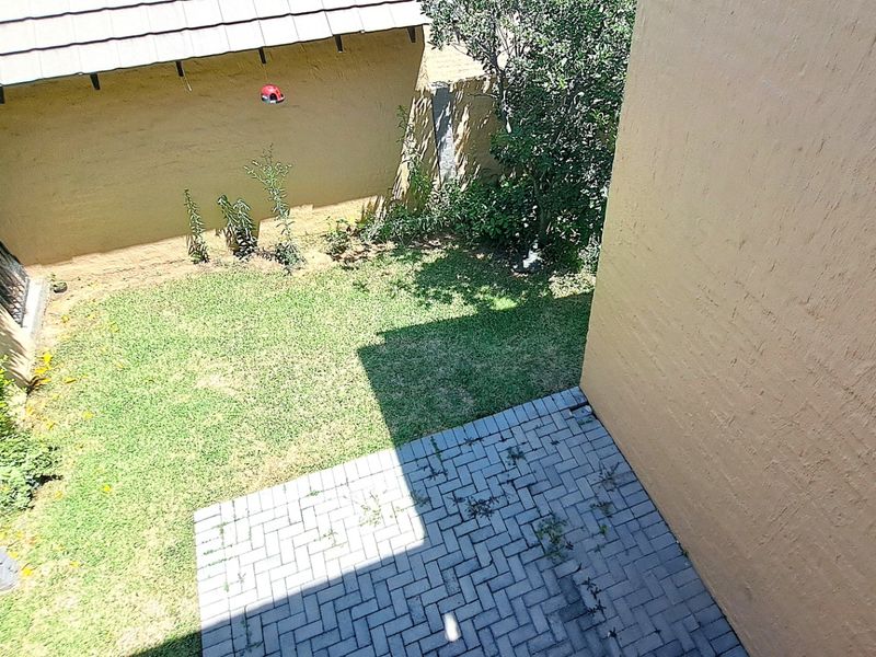 An elevated view of a private rear garden featuring a paved patio area and a small lawn enclosed by boundary walls.