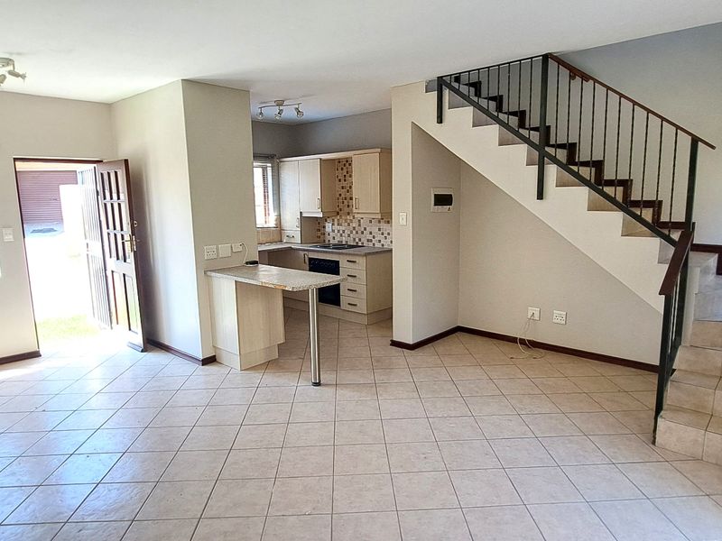 Open-plan living area featuring tiled flooring, a functional kitchen with built-in cabinetry, and a staircase leading to the upper level.