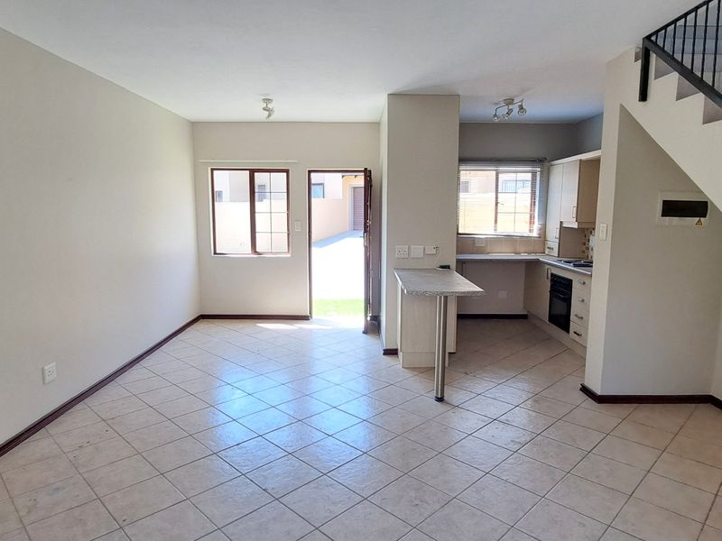 Open-plan living and kitchen area featuring tiled floors, built-in cabinetry, a breakfast counter, and a staircase leading to the upper level.