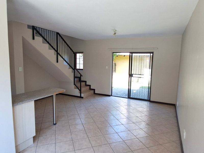 Spacious open-plan living area featuring tiled flooring, a built-in breakfast counter, and a staircase leading to the upper level with access to the patio.
