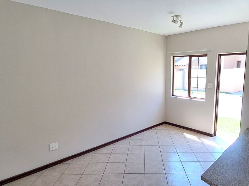 An empty open-plan living area featuring tiled flooring, neutral walls, and direct access to the exterior through a glass-paneled door.