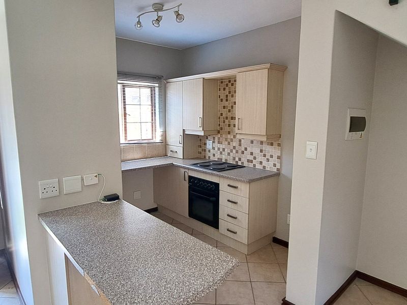 Compact kitchen featuring built-in cabinetry, laminate countertops, mosaic tile backsplash, and integrated electric oven and hob, with an adjoining breakfast nook.