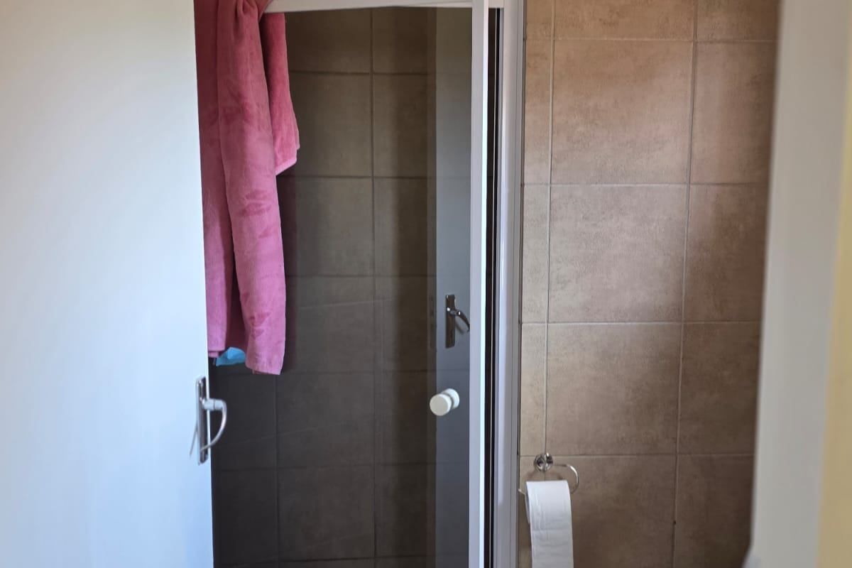 A compact bathroom featuring a shower enclosure with a glass door, a standard toilet, and tiled walls and flooring.