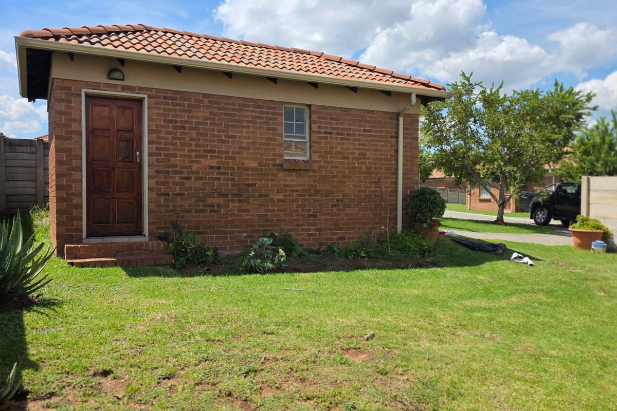 A view of the exterior rear brick facade featuring a tiled roof, wooden door, and small window, set within a private garden area.