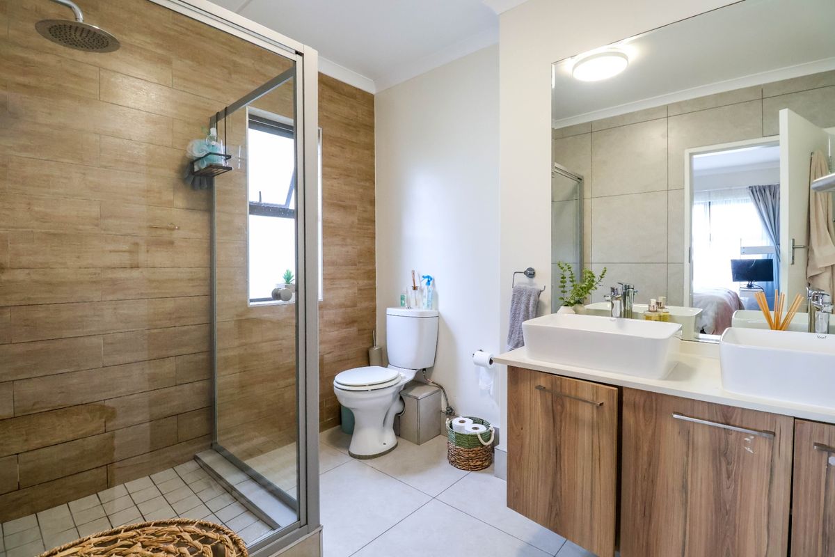 Modern bathroom featuring a walk-in shower with wood-look tiling, a double vanity with vessel sinks, and a large wall-mounted mirror.