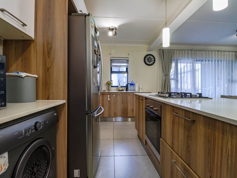 Modern kitchen featuring wood-finish cabinetry, stone countertops, a gas hob, built-in oven, and integrated laundry space with tiled flooring.