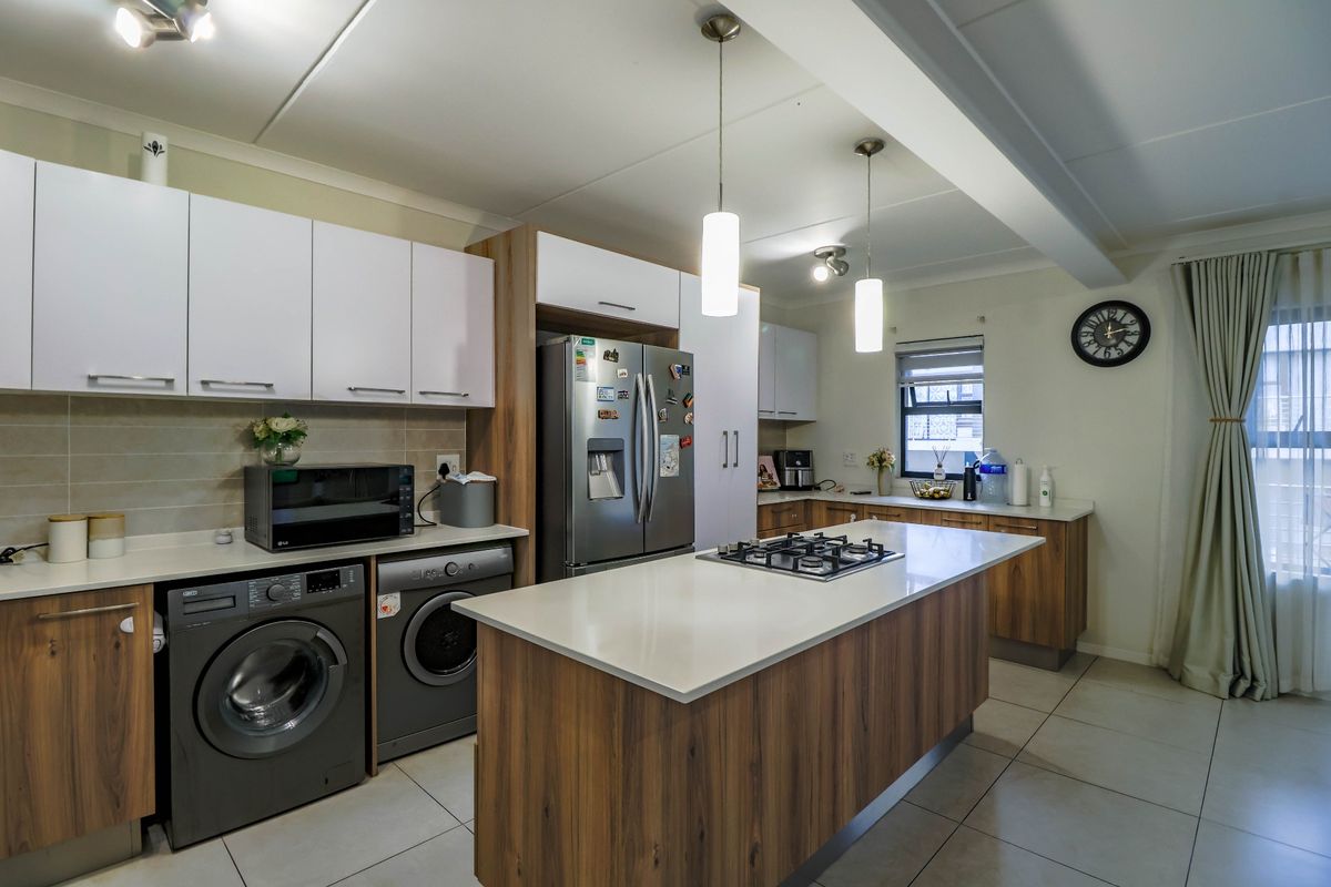 Modern kitchen featuring a central island with a gas hob, stone countertops, ample built-in cabinetry, and sleek pendant lighting.