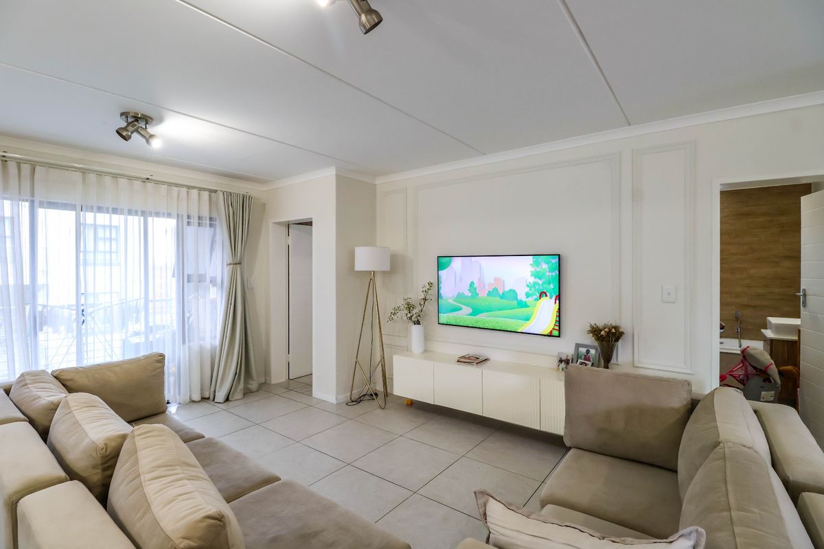 A bright and modern living room featuring tiled floors, decorative wall paneling, and a built-in media console with access to an outdoor balcony.