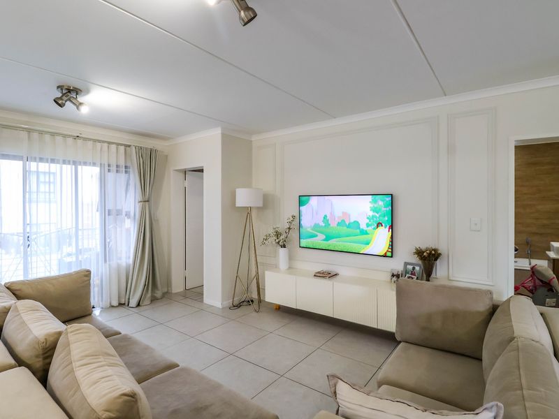 A bright and modern living room featuring tiled floors, decorative wall paneling, and a built-in media console with access to an outdoor balcony.