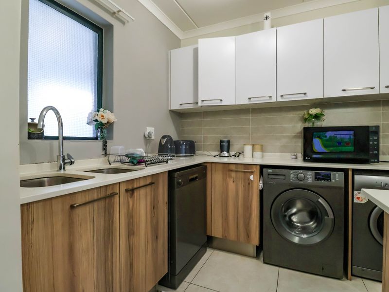 Modern kitchen featuring wood-grain lower cabinetry, white upper cabinets, stone countertops, tiled backsplash, and integrated laundry and dishwasher appliances.