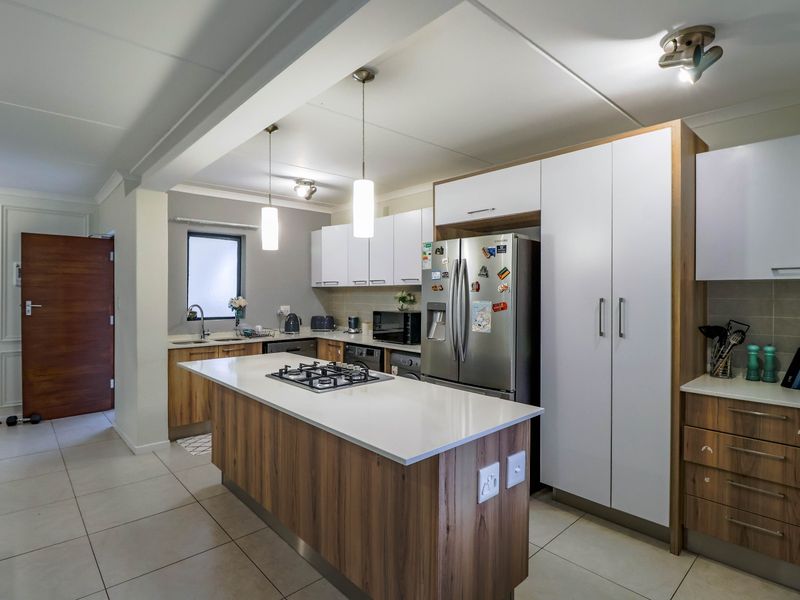 Modern kitchen featuring a central island with a gas hob, stone countertops, ample built-in cabinetry, and tiled flooring in an open-plan layout.
