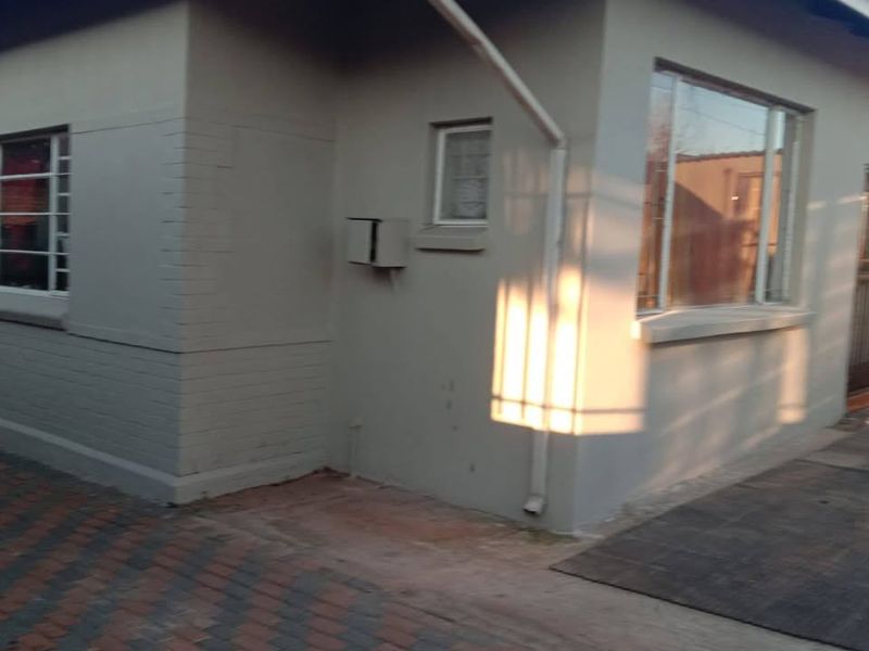 A view of the rear exterior of the house featuring painted brick walls, aluminium window frames, and paved ground area.