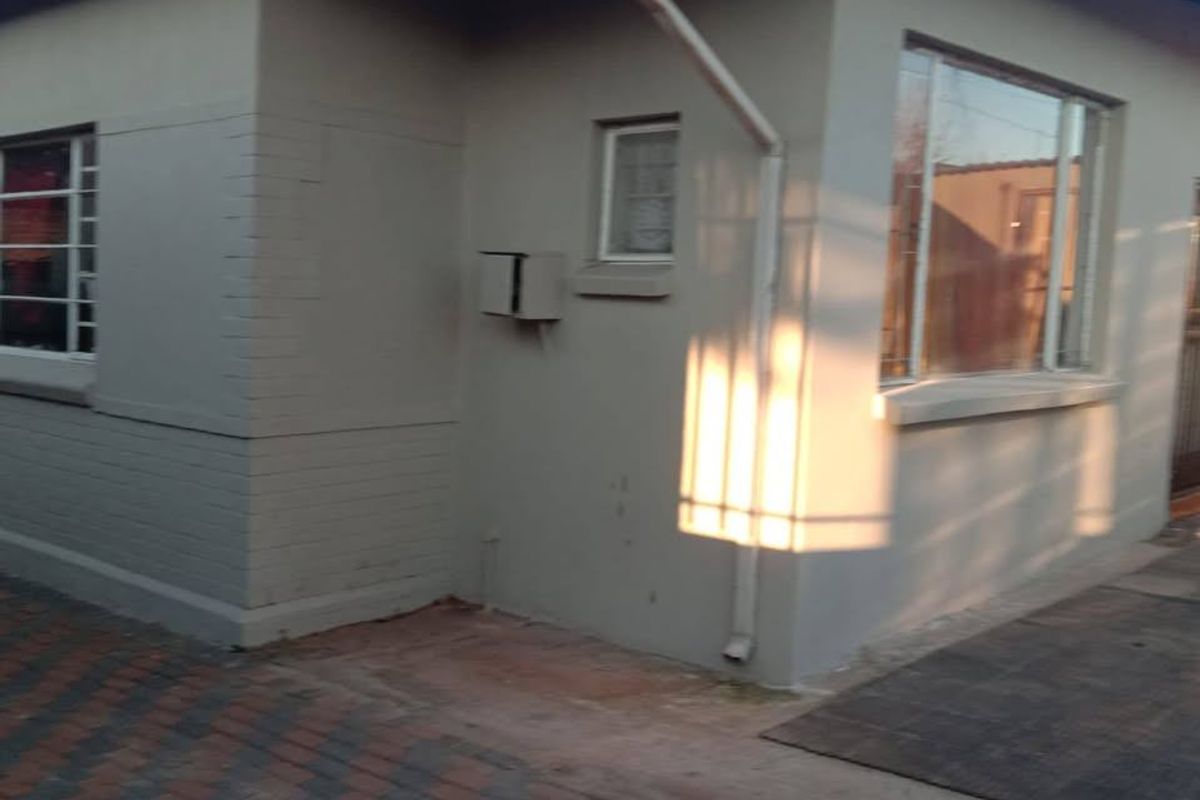 A view of the rear exterior of the house featuring painted brick walls, aluminium window frames, and paved ground area.