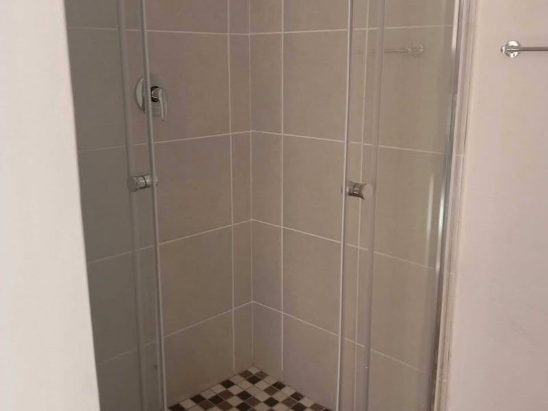 A functional shower cubicle featuring neutral wall tiling, a mosaic-tiled floor, and a glass enclosure.