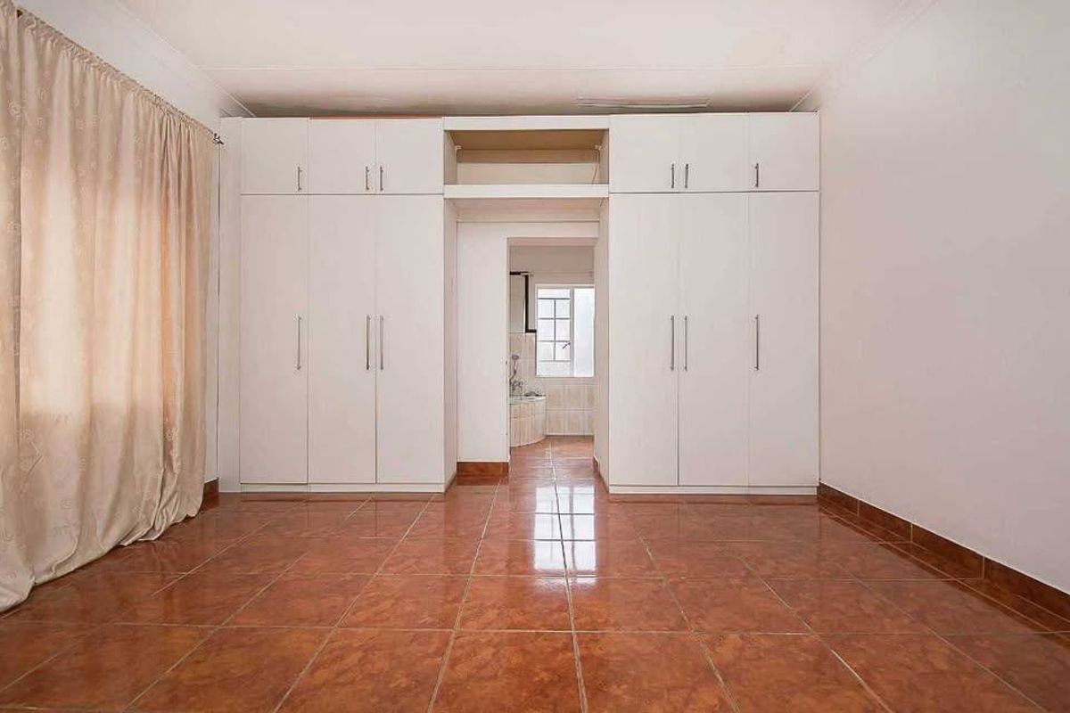 A spacious bedroom featuring extensive built-in cupboards, tiled flooring, and a neutral finish, offering a clean and functional living space.