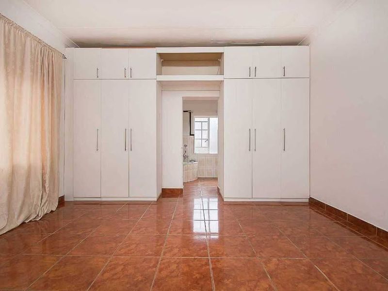 A spacious bedroom featuring extensive built-in cupboards, tiled flooring, and a neutral finish, offering a clean and functional living space.