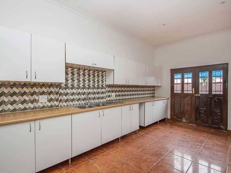 A functional kitchen featuring white built-in cabinetry, patterned tiled backsplash, double basin sink, and durable tiled flooring with direct access to the exterior.