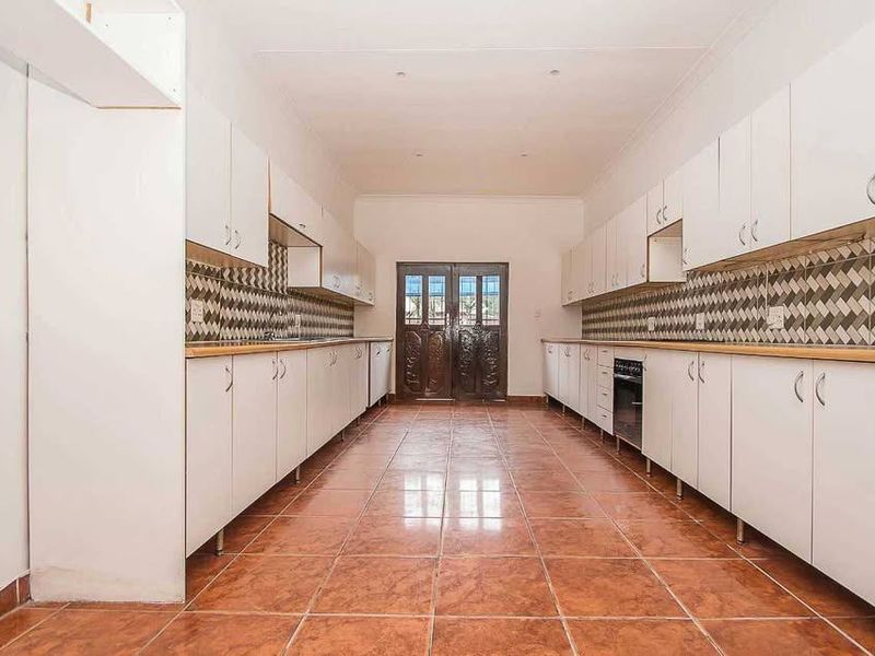 Spacious galley-style kitchen featuring extensive white cabinetry, tiled flooring, a patterned backsplash, and a built-in oven, leading to exterior double doors.