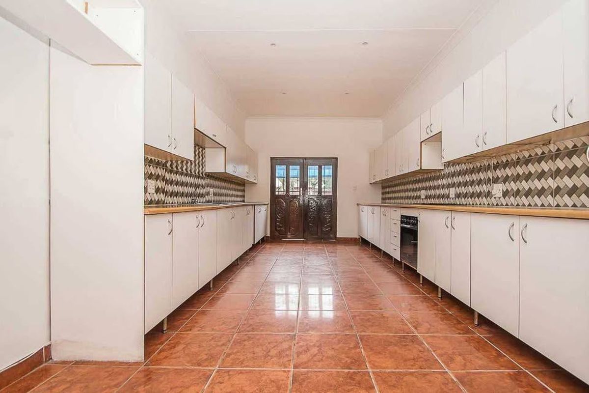 Spacious galley-style kitchen featuring extensive white cabinetry, tiled flooring, a patterned backsplash, and a built-in oven, leading to exterior double doors.