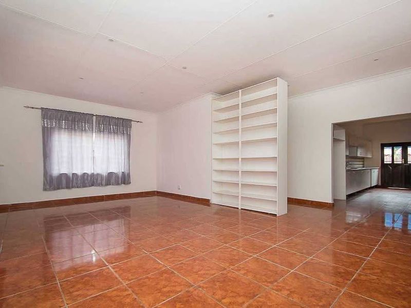 Spacious open-plan living area featuring glossy tiled flooring, a built-in shelving unit, and a convenient pass-through window connecting to the kitchen.
