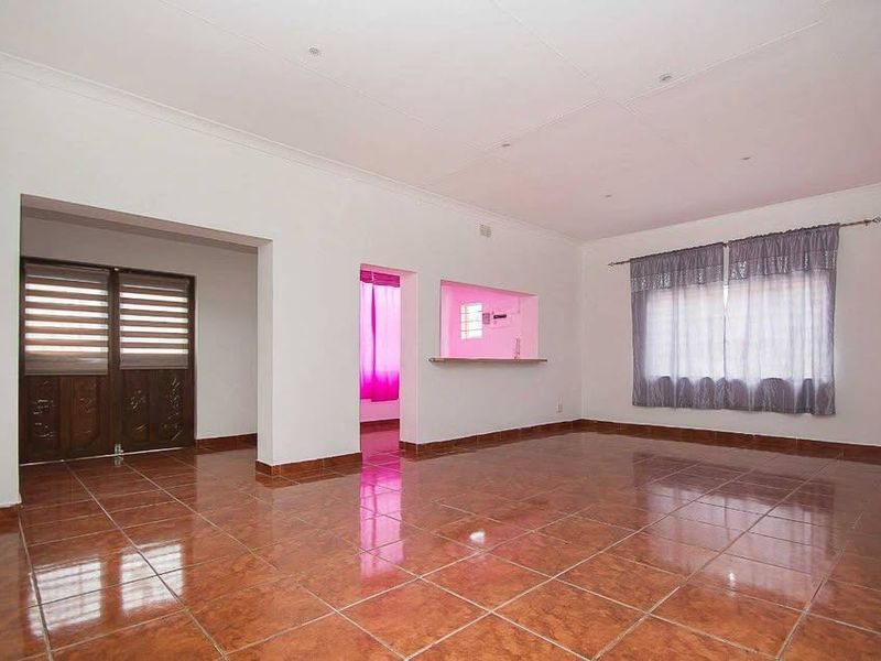 Spacious, empty living area featuring glossy tiled flooring, a convenient serving hatch to the kitchen, and neutral walls.