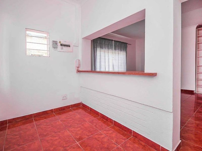 An empty living area featuring tiled flooring, a convenient serving hatch connecting to the kitchen, and built-in shelving.