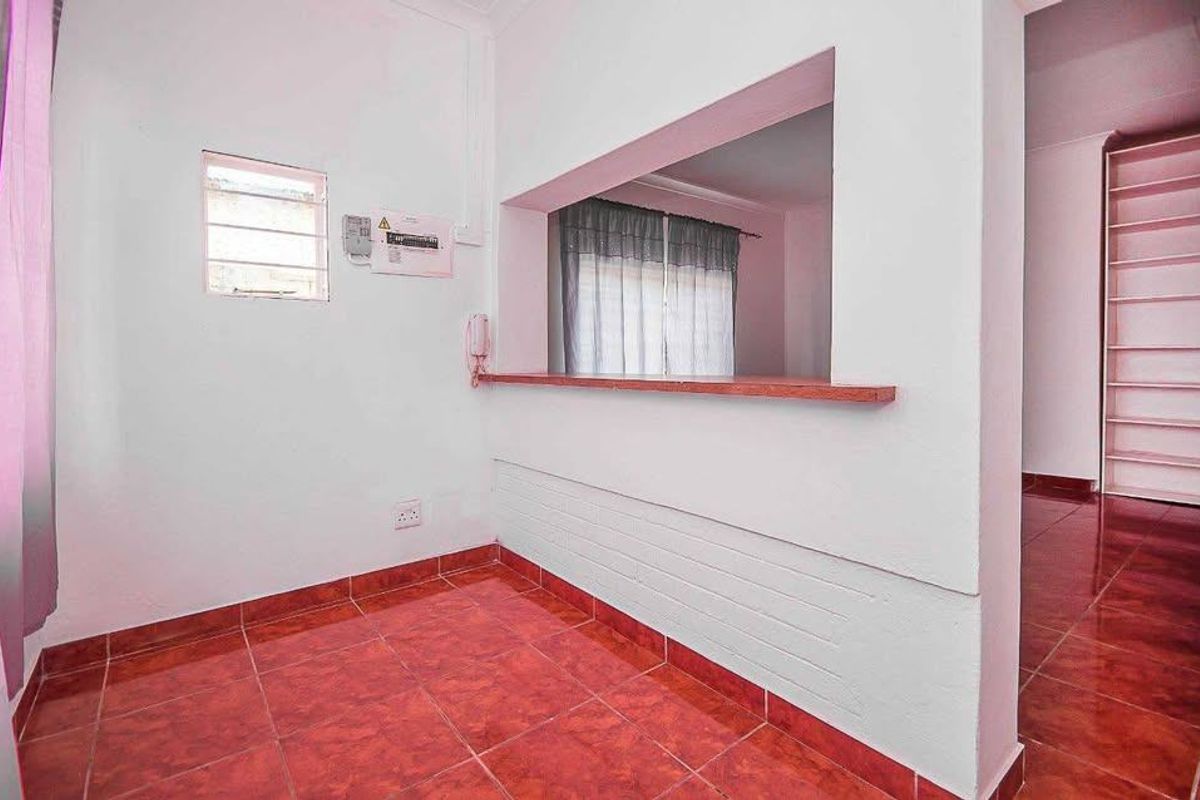 An empty living area featuring tiled flooring, a convenient serving hatch connecting to the kitchen, and built-in shelving.